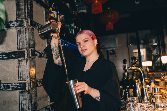 Bartender with pink hair mixing cocktails and smiling at the bar