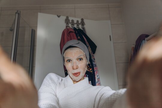Woman taking a skincare selfie with facial mask in bathroom