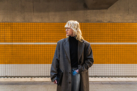 Young man in coat waiting at urban subway platform