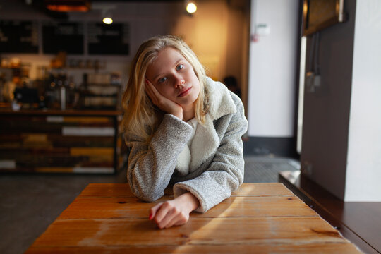 Thoughtful woman in casual clothing sitting at wooden cafe table