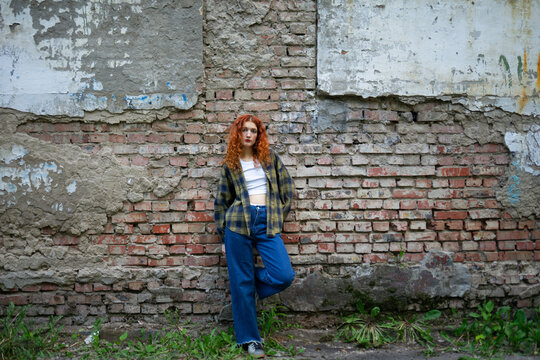 Red-haired woman in casual outfit leaning on old brick wall outdoors