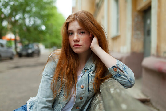 Thoughtful teenage girl with red hair leaning outdoors in summer