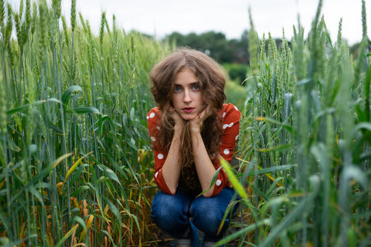 Woman with curly hair in red blouse smiling in wheat field in summer
