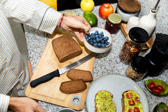 Person reparing healthy breakfast with avocado toast and fruit in kitchen