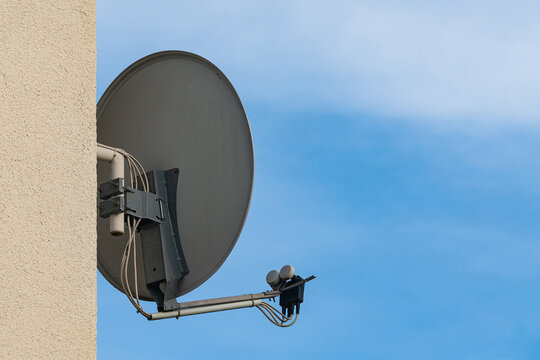 Satellite dish mounted on building wall under clear sky