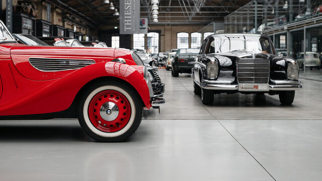 BMW 327 and Mercedes-Benz W111 in Classic Remise. Close-up side view of a red vintage BMW 327 and a classic Mercedes-Benz W111 parked in the hall of Classic Remise in Berlin, Germany - January 14 2026