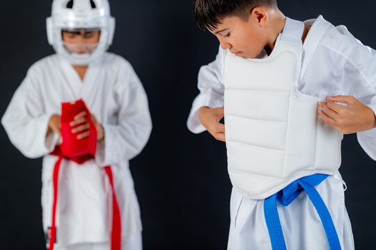 Two boys wearing protective sparring gear practicing karate in studio with black background. Highlights safety, control, and disciplined martial arts movement.