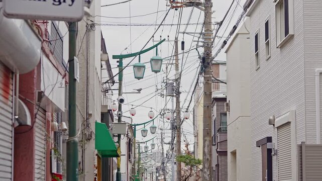 An eye-level shot capturing the unique atmosphere of a quiet Japanese residential alley with complex overhead wiring and traditional houses.