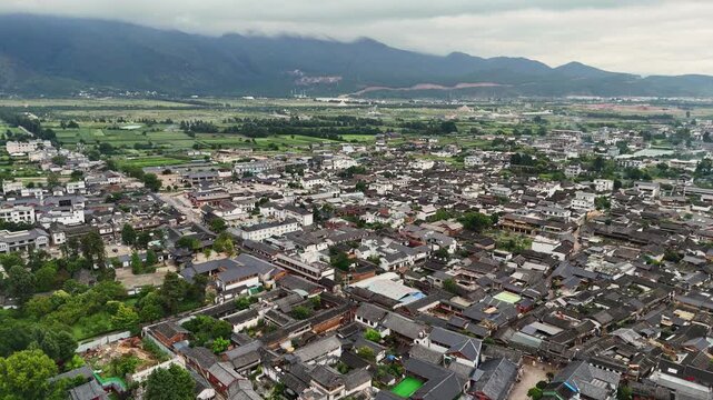 Baisha town traditional houses and farmland with mountains and clouds near Fuguo Monastery Yunnan, aerial backdrop