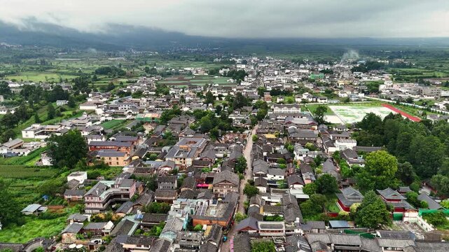 Baisha town rooftops and narrow streets with farmland and mountains near Fuguo Monastery Yunnan, aerial tracking along road