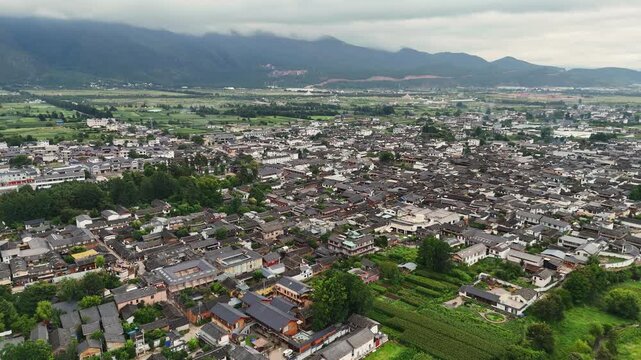 Baisha town rooftops and surrounding farmland with mountain range near Fuguo Monastery Yunnan, aerial establishing overview
