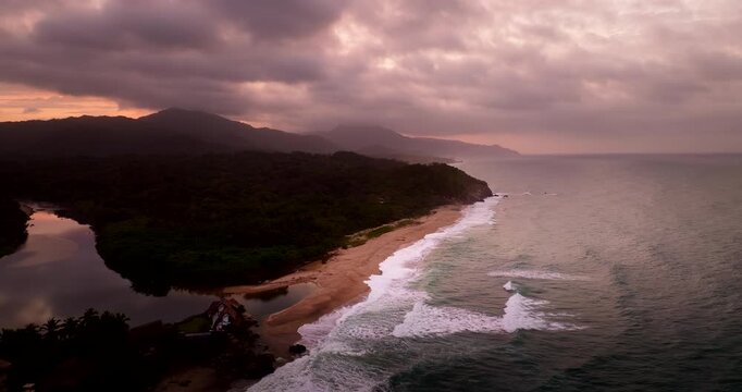 Coastline, jungle, and waves at Los Naranjos beach near Tayrona National Park during a dramatic sunset in Colombia. Aerial drone view, copy space