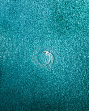 Aerial view of a boat sailing through the crystal-clear turquoise waters, leaving a swirling wake in its path, Noumea, New Caledonia.