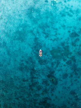 Aerial view of a solitary boat cutting through the mesmerizing turquoise waters, creating a stunning contrast against the clear sea bottom, Noumea, New Caledonia.