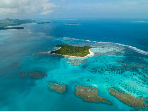 Aerial view of a vibrant turquoise sea surrounding a lush green island, with coral reefs creating mesmerizing patterns in the clear waters, Noumea, New Caledonia.