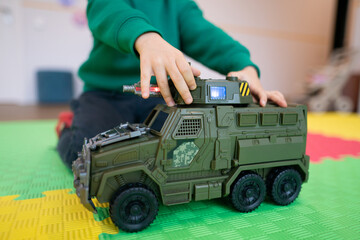 Child playing with a green toy military vehicle on a colorful mat © Tsyb Oleh