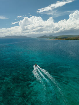Aerial view of a boat gliding through the turquoise waters, leaving a frothy white trail against the backdrop of distant islands, Noumea, New Caledonia.