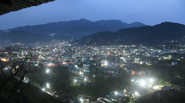 Timelapse view of a mountain city transitioning from night to early morning. City lights glowing in darkness gradually fade as natural daylight reveals hills, buildings, and landscape. Concept of time