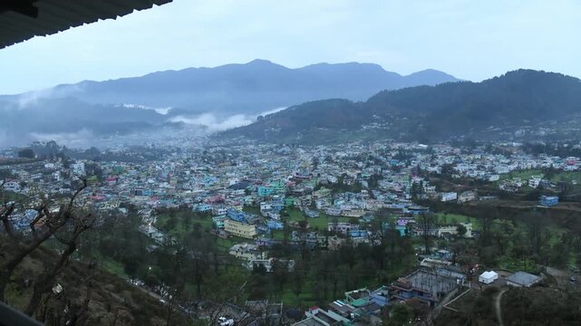 Scenic morning view of a hill town surrounded by mountains with low clouds and mist drifting over the valley. Fresh daylight reveals colorful houses, greenery, and natural landscape, ideal for travel,