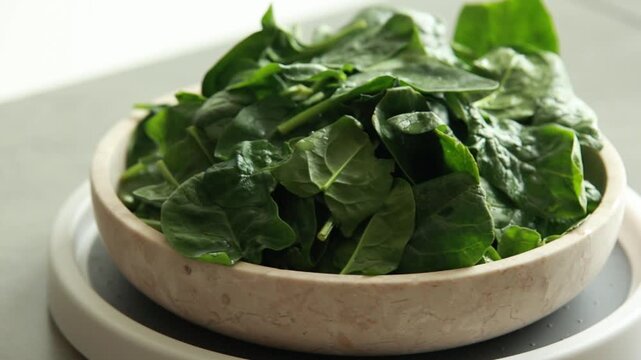 Close-up of fresh, raw baby spinach leaves in a white ceramic bowl, natural light