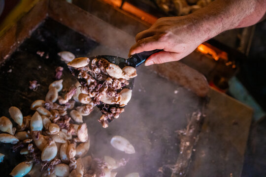 View of the succulent squid sizzling on a hot plate, smoke swirling as a spatula lifts the delectable seafood, a culinary dance of flavors, Pula, Istria County, Croatia.