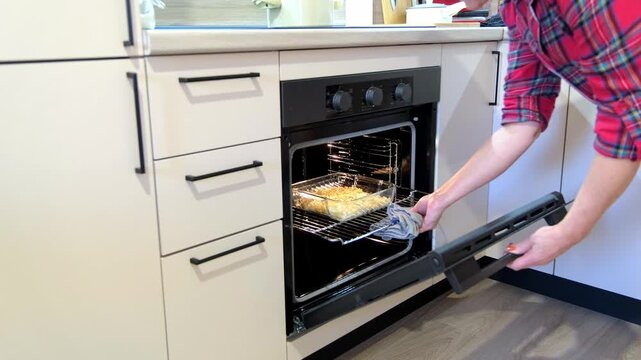 Cook retrieves tray safely. Home chef safely pulls tray out. Person carefully removes hot tray from oven. Individual gently pulls hot baking dish from oven with caution