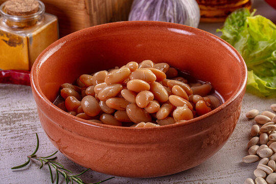 Cooked white beans in a terracotta bowl with fresh vegetables and spices.
