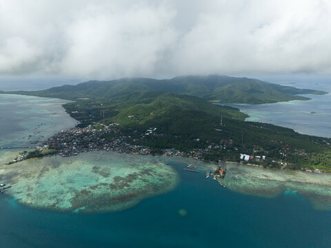 Aerial view of a lush island with turquoise waters lapping against the shore, houses dotting the coastline, Karimunjawa, Central Java, Indonesia.