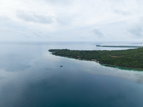 Aerial view of a boat sailing near a lush green island under a cloudy sky, Karimunjawa, Central Java, Indonesia.