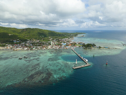 Aerial view of a pier stretching out into the turquoise sea from a vibrant coastal town nestled beneath verdant hills, Karimunjawa, Central Java, Indonesia.