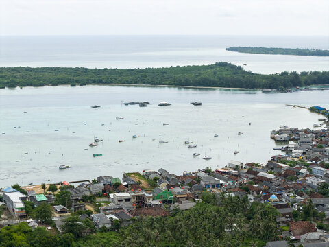 Aerial view of the turquoise waters speckled with boats contrast against the dense green islands and the vibrant village hugging the coastline, Karimunjawa, Central Java, Indonesia.