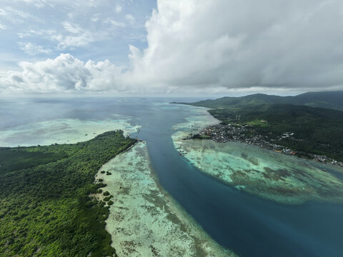 Aerial view of the turquoise waters embrace the lush green islands, meeting at the horizon under a sky brushed with clouds, Karimunjawa, Central Java, Indonesia.