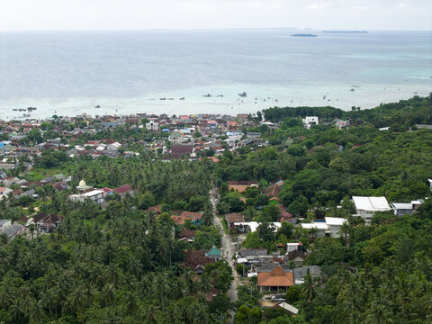 Aerial view of a lush landscape meeting the turquoise sea, dotted with buildings and trees, Karimunjawa, Central Java, Indonesia.