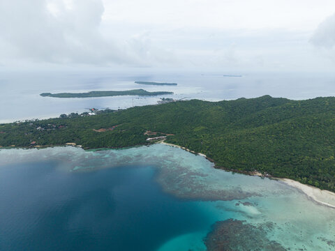 Aerial view of turquoise waters meeting the verdant coastline, a symphony of blues and greens under a vast sky, Karimunjawa, Central Java, Indonesia.