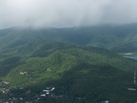 Aerial view of dense, verdant hills rolling towards the horizon under a blanket of soft, low-hanging clouds, Karimunjawa, Central Java, Indonesia.