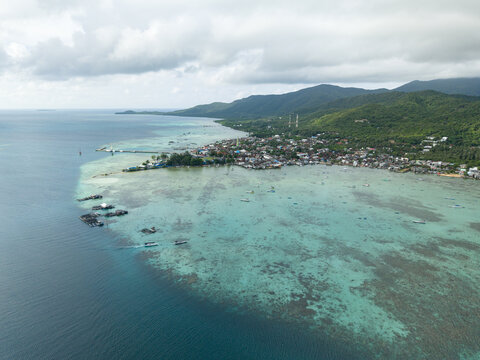 Aerial view of the shimmering turquoise waters meeting the lush green coastline, revealing the town's sprawl, Karimunjawa, Central Java, Indonesia.