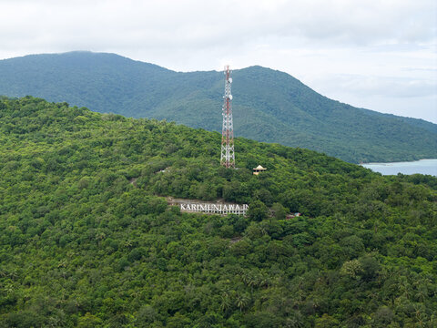 Aerial view of a telecommunications tower rising amidst the verdant hills, overlooking the 'Karimunjawa' sign nestled in the lush greenery, Karimunjawa, Central Java, Indonesia.