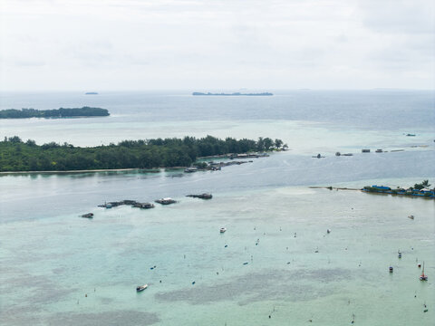 Aerial view of turquoise waters meet lush green islands, a serene seascape dotted with stilt houses and boats, Karimunjawa, Central Java, Indonesia.