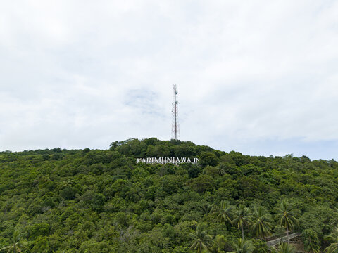 Aerial view of lush green hill crowned with the sign "KARIMUNJAWA I" and a telecommunications tower piercing the skyline, Karimunjawa, Central Java, Indonesia.