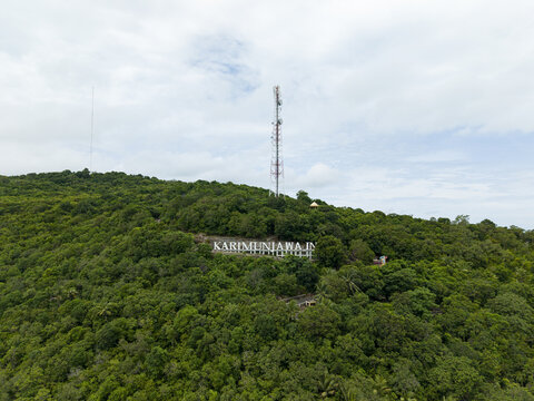 Aerial view of lush green hill displaying the name 'Karimunjawa' under a cloudy sky, Karimunjawa, Central Java, Indonesia.
