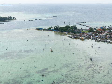 Aerial view of a coastal village nestled against turquoise waters, with fishing boats scattered across the sea, Karimunjawa, Central Java, Indonesia.