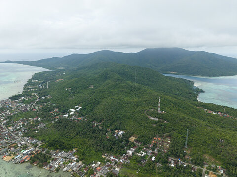 Aerial view of a lush island paradise where emerald forests meet turquoise waters, dotted with structures and towers, Karimunjawa, Central Java, Indonesia.