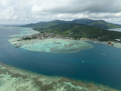 Aerial view of the vibrant turquoise waters surrounding a lush island dotted with buildings, a stark contrast to the deep blue sea, Karimunjawa, Central Java, Indonesia.
