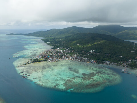 Aerial view of a vibrant village nestled amidst turquoise waters and lush greenery, framed by distant mountains, Karimunjawa, Central Java, Indonesia.