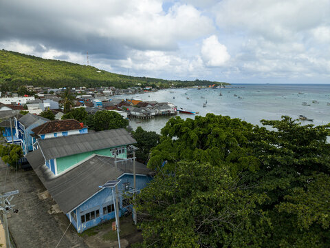 Aerial view of the coastal town meeting the turquoise sea under a sky brushed with grey and white, Karimunjawa, Central Java, Indonesia.