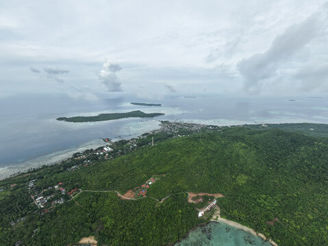 Aerial view of the island's lush green landscape meeting the turquoise waters under a vast sky, Karimunjawa, Central Java, Indonesia.