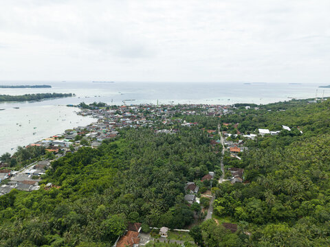 Aerial view of emerald trees meet the coastlines, the town's buildings nestled between the lush greenery and the vast ocean, Karimunjawa, Central Java, Indonesia.