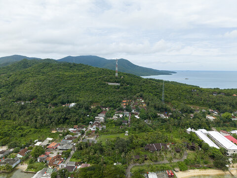 Aerial view of lush green hills cascading into the turquoise waters of the sea, punctuated by a small coastal village, Karimunjawa, Central Java, Indonesia.