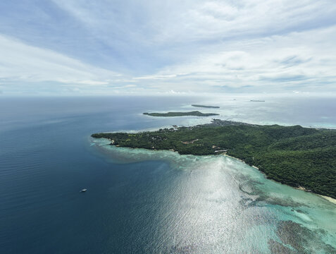 Aerial view of the coastline where the deep blue sea meets the white sandy beach and lush green forest, Karimunjawa, Central Java, Indonesia.