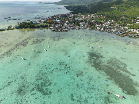 Aerial view of boats scattered on shallow turquoise waters near a densely populated shoreline, Karimunjawa, Central Java, Indonesia.